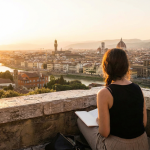 Femme adulte prenant des notes face à un paysage urbain au coucher du soleil pendant son voyage linguistique CPF.