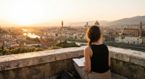 Femme adulte prenant des notes face à un paysage urbain au coucher du soleil pendant son voyage linguistique CPF.