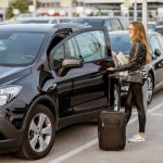 Jeune femme avec une valise récupérant sa location voiture Héraklion sur un parking.